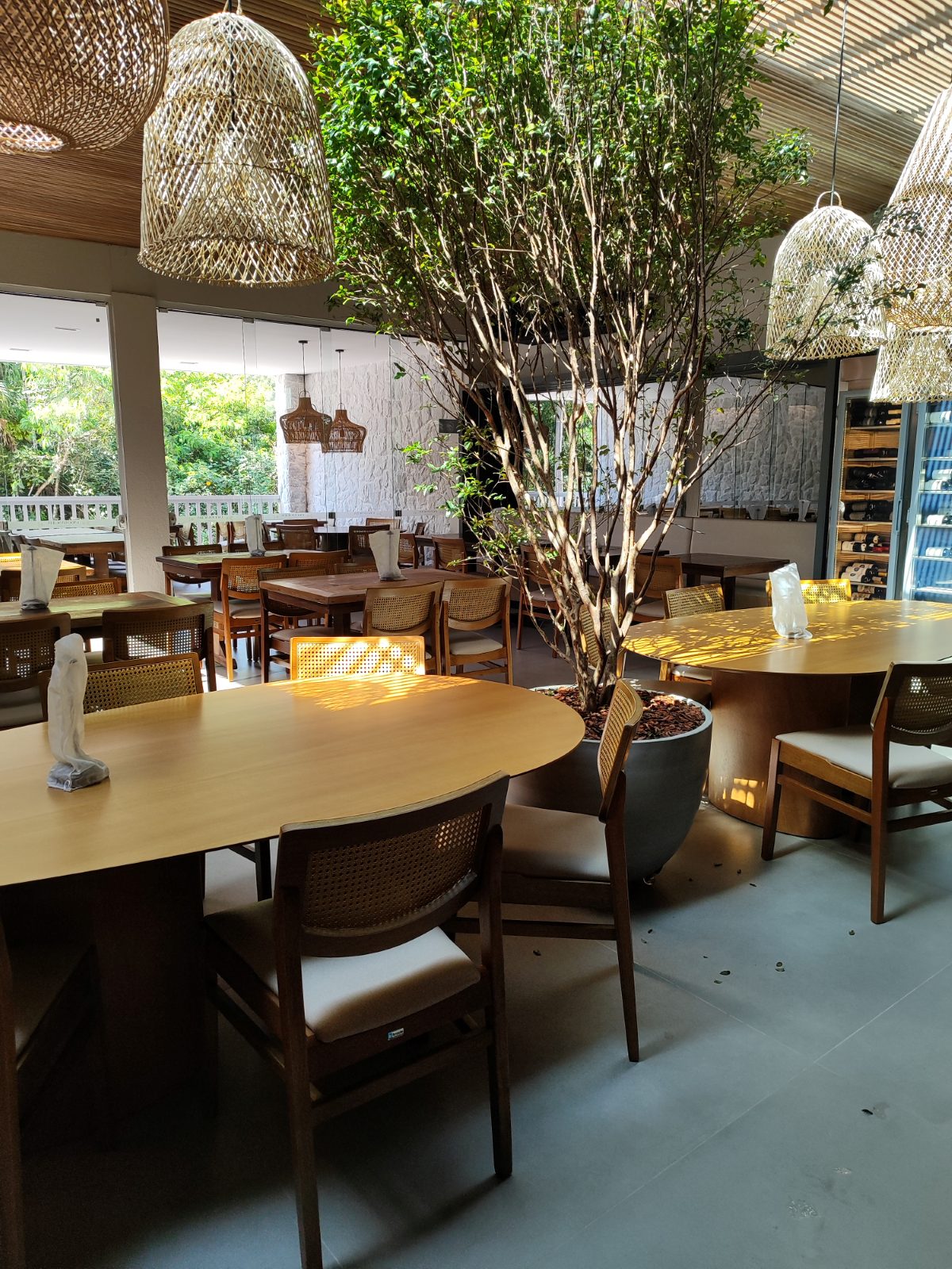 Restaurante com mesas de madeira, cadeiras com encosto de palhinha e luminárias de fibra