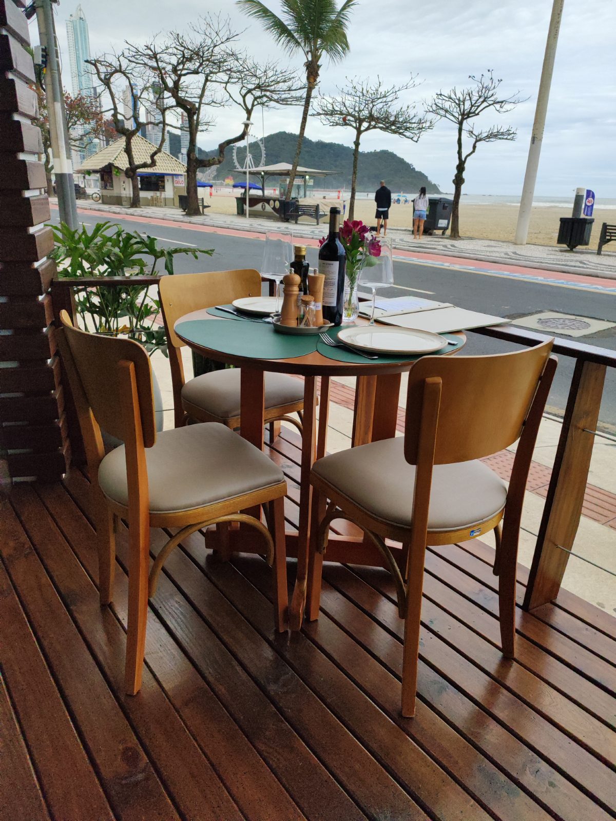 Deck de restaurante à beira-mar com mesa redonda e cadeiras de madeira
