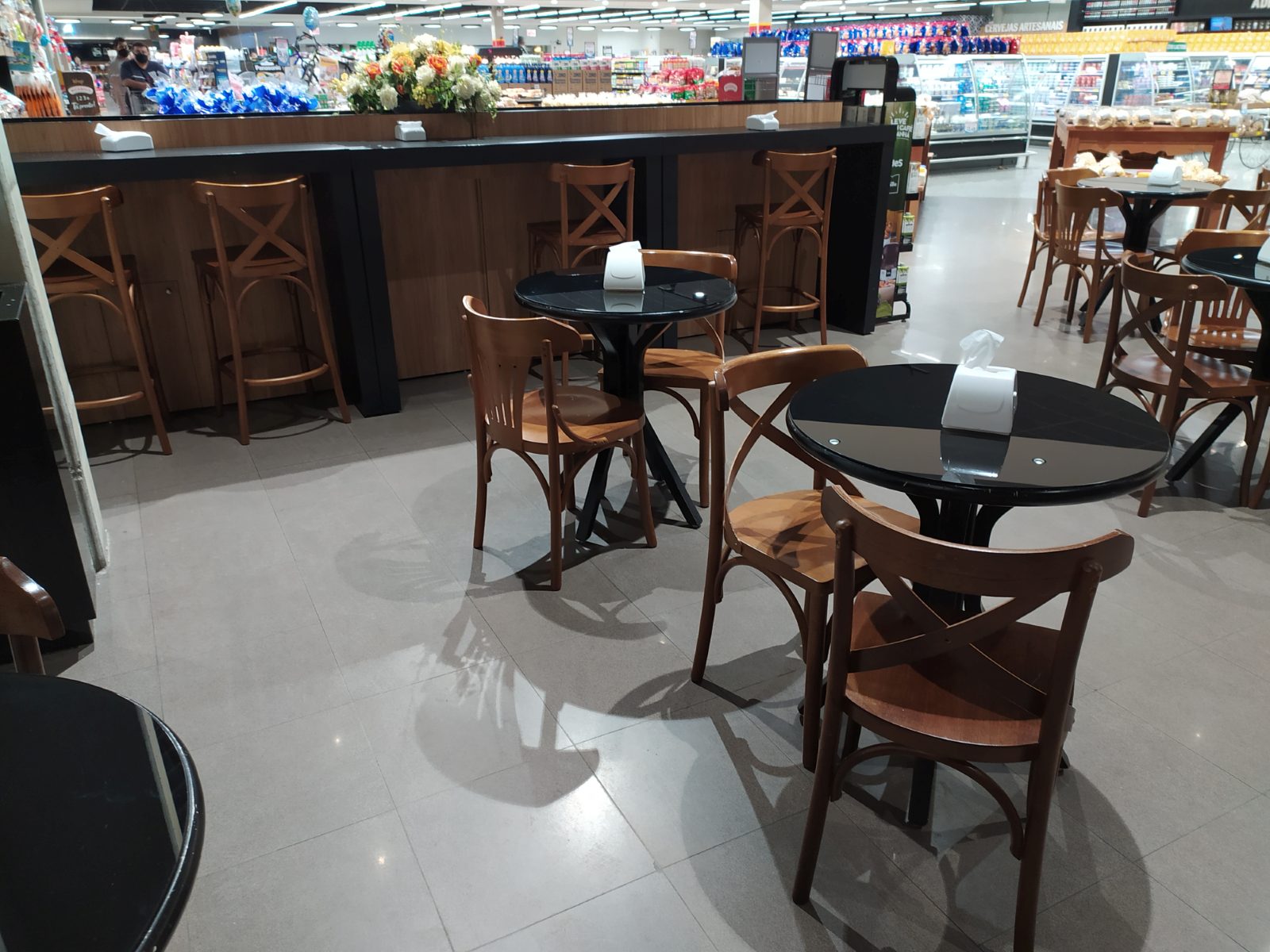 Espaço de café em mercado com mesas redondas e cadeiras de madeira
